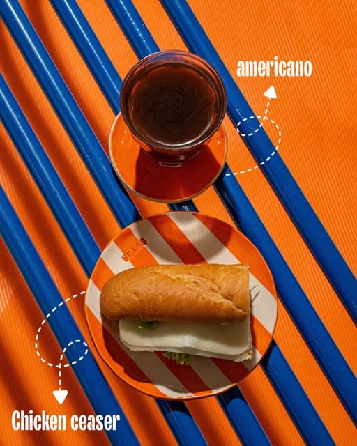 An Americano and a chicken Caesar sandwich on blue and orange stripes